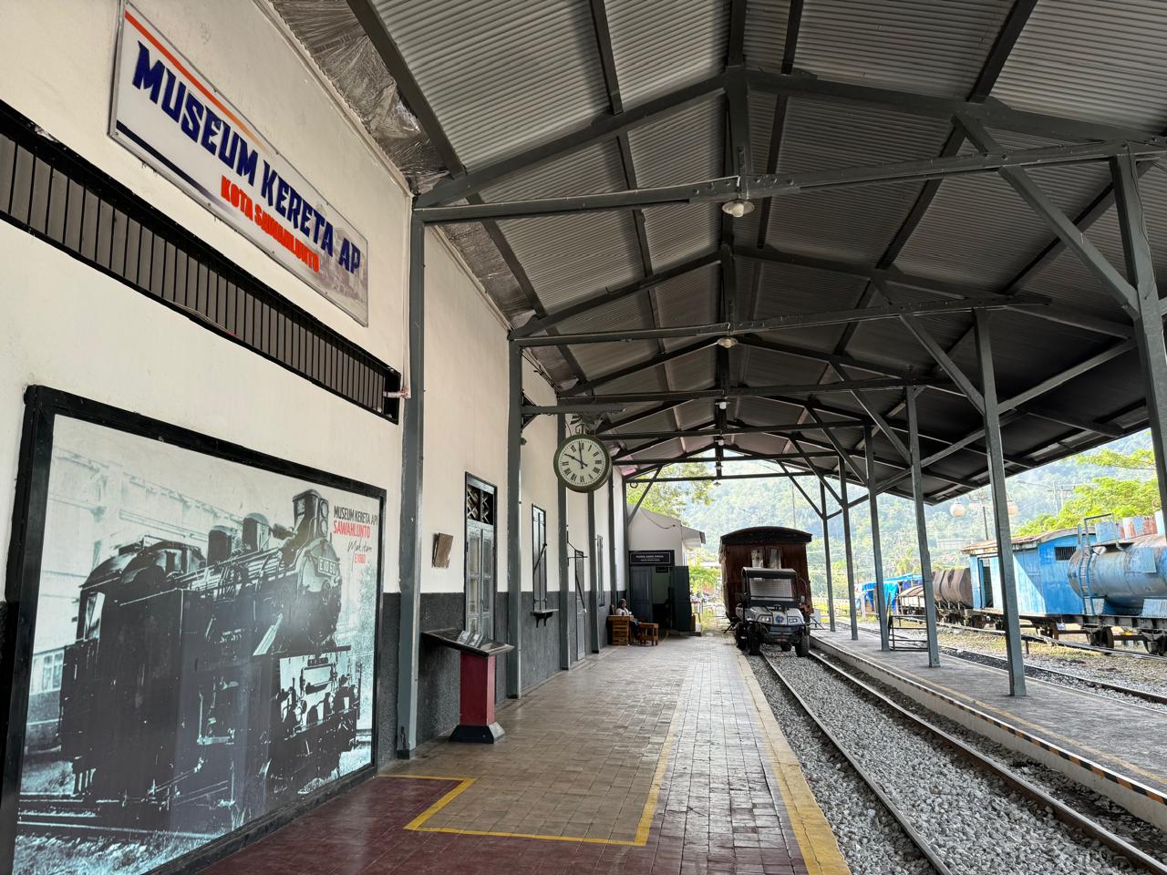 Interior view of the Sawahlunto Train Museum in West Sumatra, showcasing vintage locomotives, old railway tracks, and historical photographs under a covered platform.